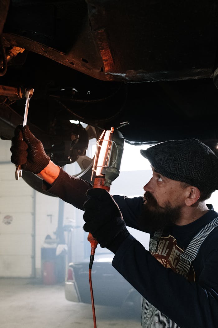A bearded auto mechanic working diligently under a car in a garage.